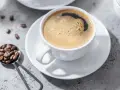 Aromatic coffee in a white cup, with beans on a spoon. Czy kawa jest lekkostrawna? To zależy od sposobu parzenia.