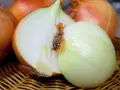 Pot o zapachu cebuli, z przekrojoną na pół białą cebulą i kilkoma całymi w tle, leżą na wiklinowym koszyku.