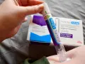 Ręka trzymająca pen do podawania zastrzyków na cukrzycę Trulicity 1,5 mg. W tle pudełko leku.