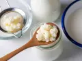 Kefir na kaca to naturalny sposób na regenerację. Ziarna kefirowe na łyżce, sitko i naczynia z mlekiem sugerują domową produkcję.