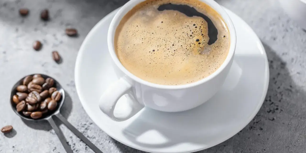 Aromatic coffee in a white cup, with beans on a spoon. Czy kawa jest lekkostrawna? To zależy od sposobu parzenia.