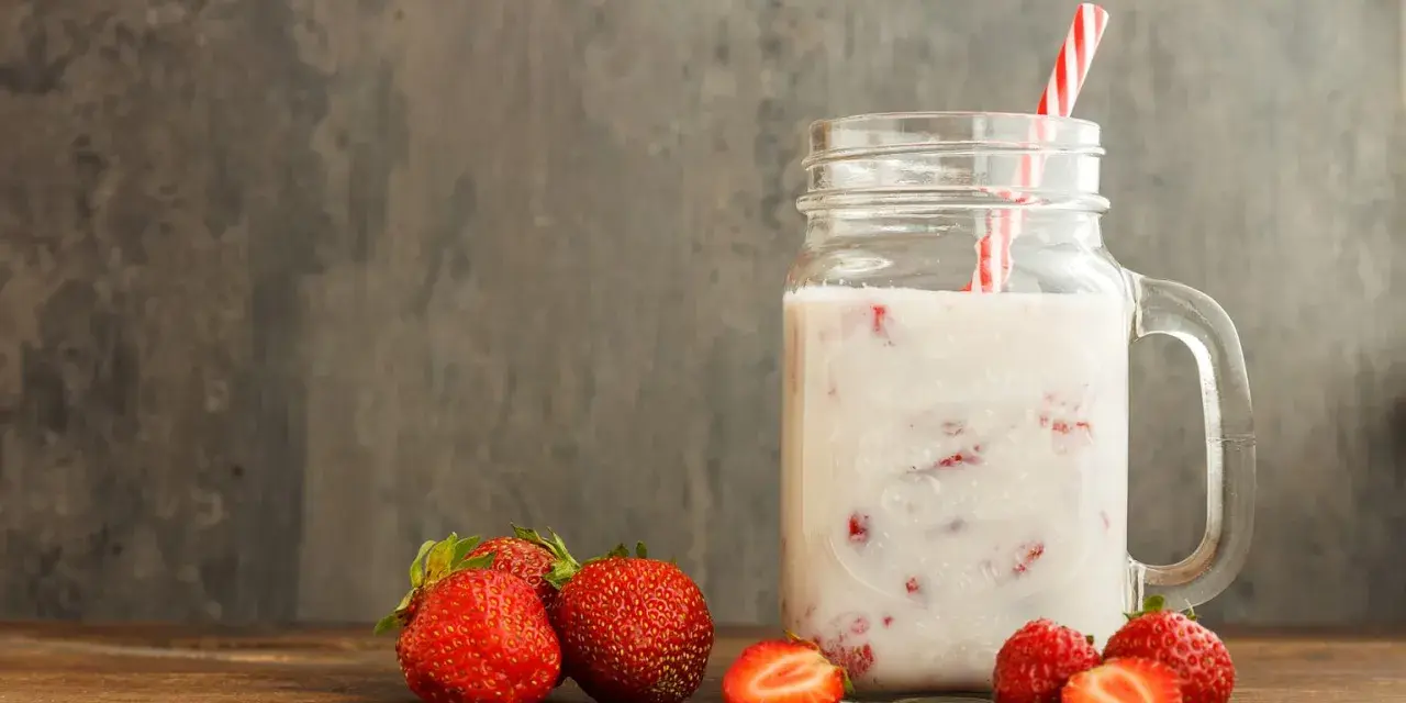 Kefir z truskawkami w słoiku, obok świeże owoce. Niska wartość indeksu glikemicznego sprawia, że to zdrowa przekąska.