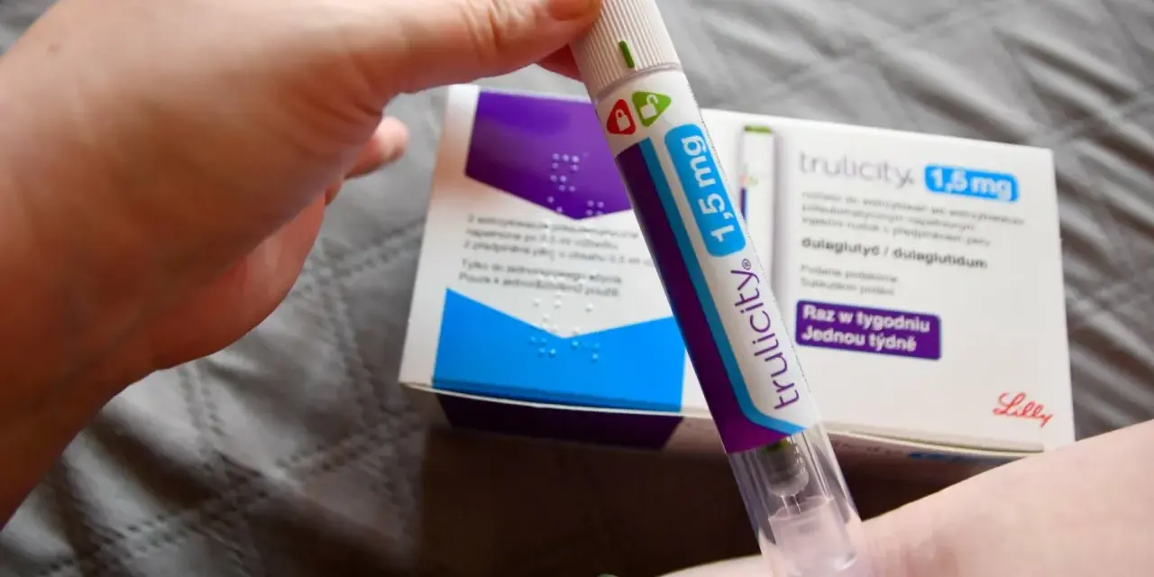 Ręka trzymająca pen do podawania zastrzyków na cukrzycę Trulicity 1,5 mg. W tle pudełko leku.