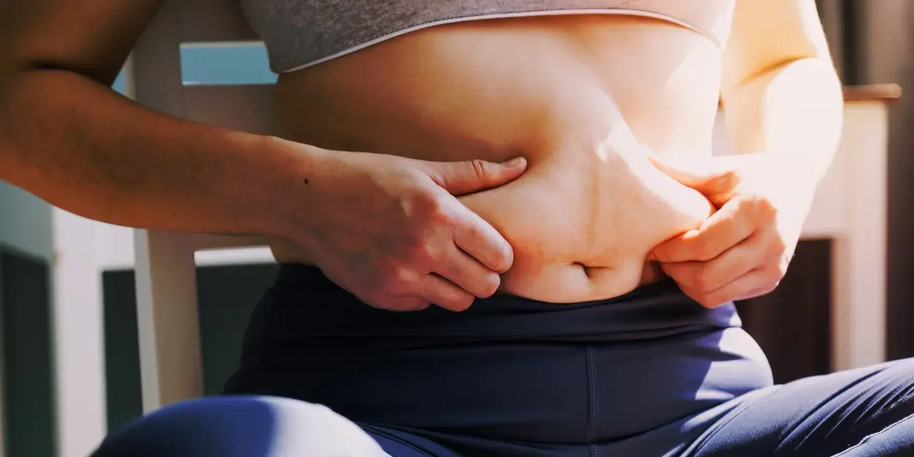 Kobieta chwyta fałd tłuszczu na brzuchu, zastanawiając się, jak schudnąć 4 kg.