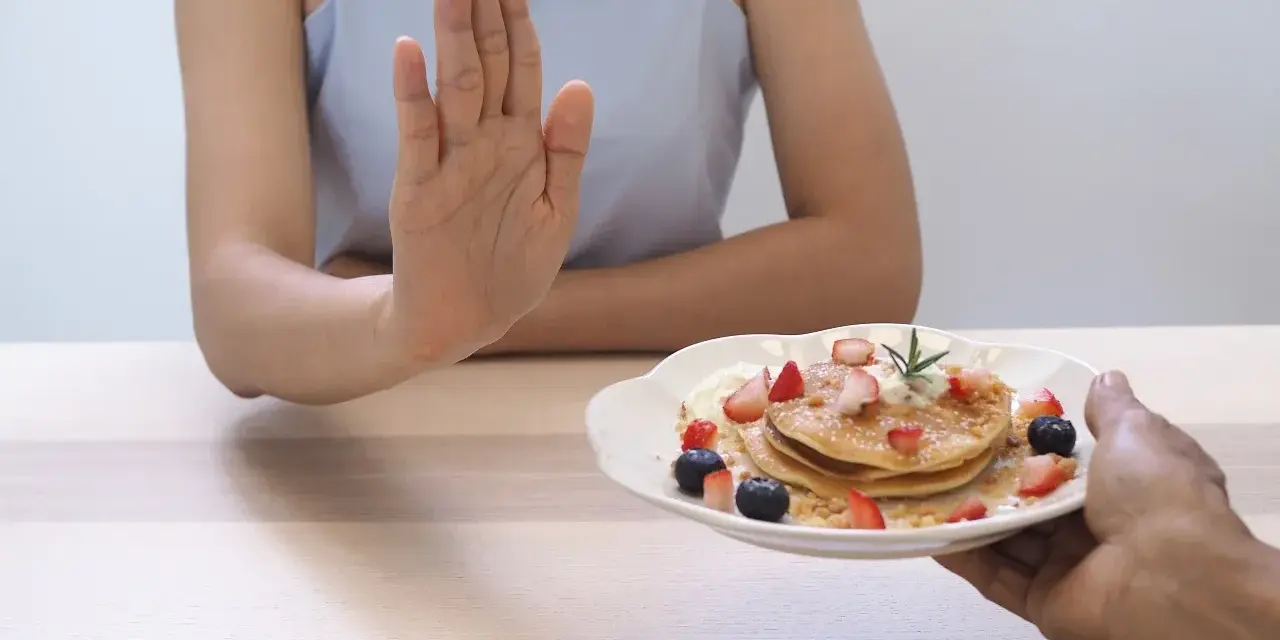 Dłoń odrzuca talerz z naleśnikami i owocami. To symboliczne przedstawienie, jak dieta 1200 kcal efekty po 2 tygodniach motywuje do zdrowych wyborów.