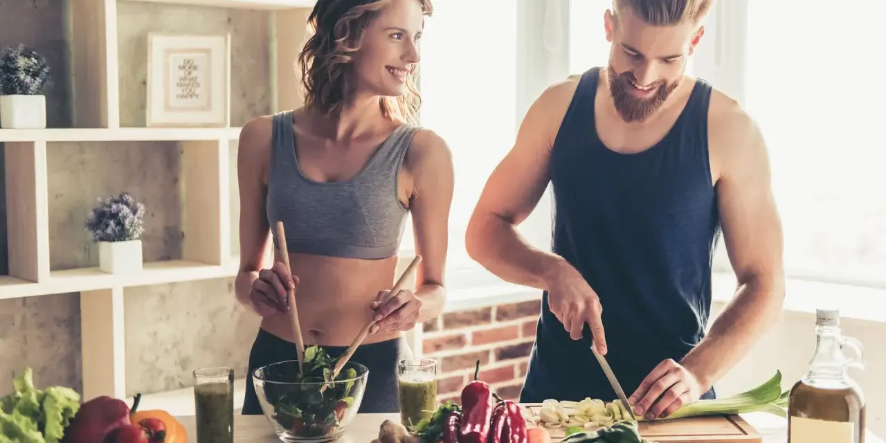 Para dieta 3000 kcal jadłospis tygodniowy, para przygotowuje zdrowe posiłki. Ona miesza sałatkę, on kroi warzywa.