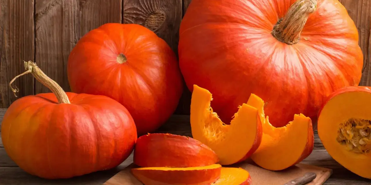 Pomarańczowe dynie, w tym połówka i kawałki na desce, przypominają o ich bogactwie witamin i cennych właściwościach zdrowotnych.