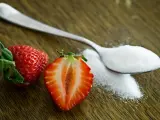 Łyżeczka białego proszku, przypominającego cukier, obok przekrojonej truskawki. Czy to stewia, co to jest?