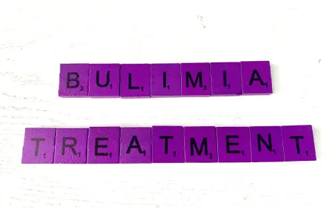 Fioletowe kafelki z literami układają słowa "BULIMIA TREATMENT". Bulimia co to? Leczenie jest kluczowe.