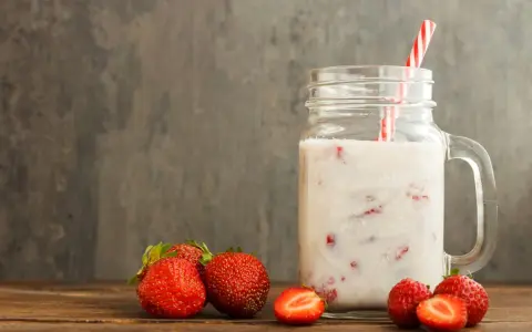 Kefir z truskawkami w słoiku, obok świeże owoce. Niska wartość indeksu glikemicznego sprawia, że to zdrowa przekąska.