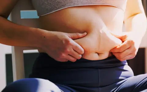 Kobieta chwyta fałd tłuszczu na brzuchu, zastanawiając się, jak schudnąć 4 kg.