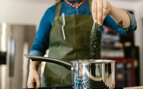 Kobieta w fartuchu dodaje sól do garnka, zastanawiając się, ile sodu dziennie jest bezpieczne.