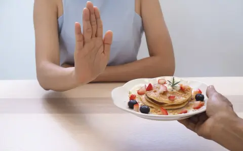 Dłoń odrzuca talerz z naleśnikami i owocami. To symboliczne przedstawienie, jak dieta 1200 kcal efekty po 2 tygodniach motywuje do zdrowych wyborów.