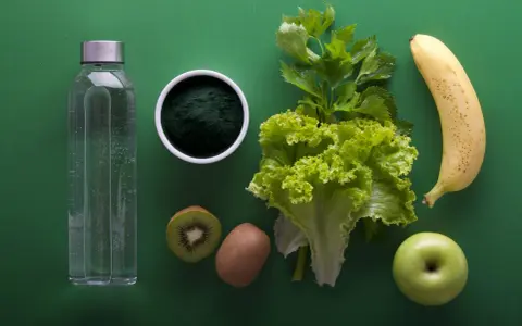 Składniki na japońską dietę wodną: butelka wody, spirulina, kiwi, sałata, seler, banan i jabłko.