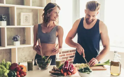Para dieta 3000 kcal jadłospis tygodniowy, para przygotowuje zdrowe posiłki. Ona miesza sałatkę, on kroi warzywa.