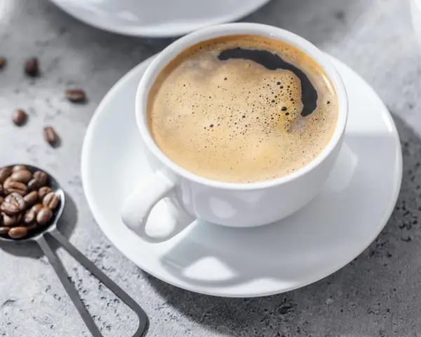 Aromatic coffee in a white cup, with beans on a spoon. Czy kawa jest lekkostrawna? To zależy od sposobu parzenia.