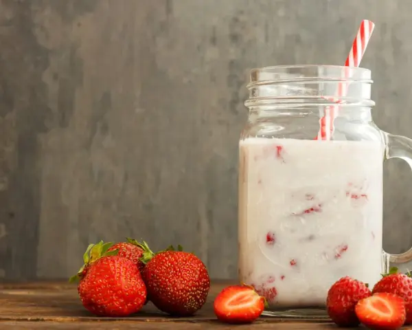 Kefir z truskawkami w słoiku, obok świeże owoce. Niska wartość indeksu glikemicznego sprawia, że to zdrowa przekąska.