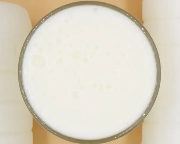 Szklanka pełna pianistego kefiru, otoczona białymi butelkami. Idealny moment, kiedy pić kefir, to teraz!