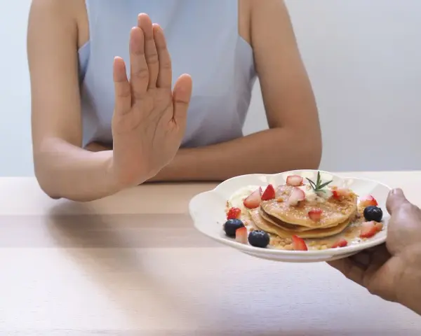 Dłoń odrzuca talerz z naleśnikami i owocami. To symboliczne przedstawienie, jak dieta 1200 kcal efekty po 2 tygodniach motywuje do zdrowych wyborów.