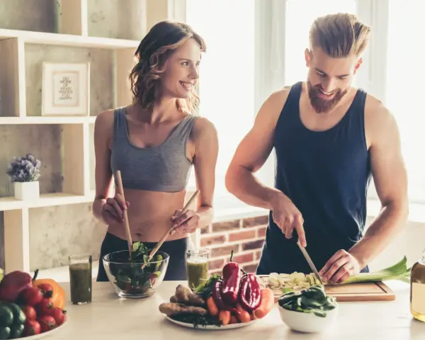 Para dieta 3000 kcal jadłospis tygodniowy, para przygotowuje zdrowe posiłki. Ona miesza sałatkę, on kroi warzywa.