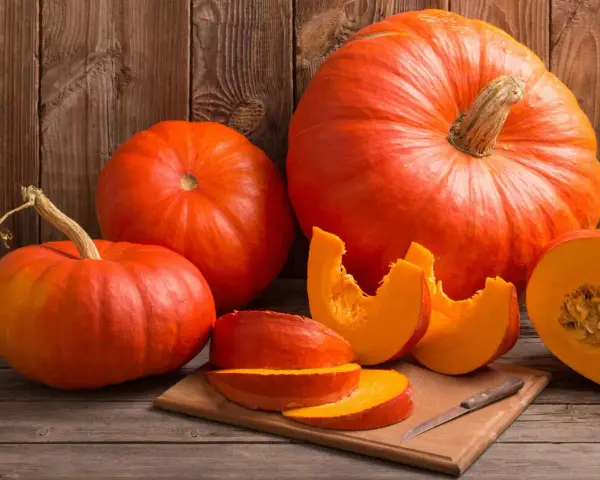 Pomarańczowe dynie, w tym połówka i kawałki na desce, przypominają o ich bogactwie witamin i cennych właściwościach zdrowotnych.