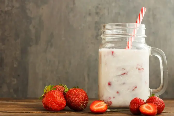 Kefir z truskawkami w słoiku, obok świeże owoce. Niska wartość indeksu glikemicznego sprawia, że to zdrowa przekąska.