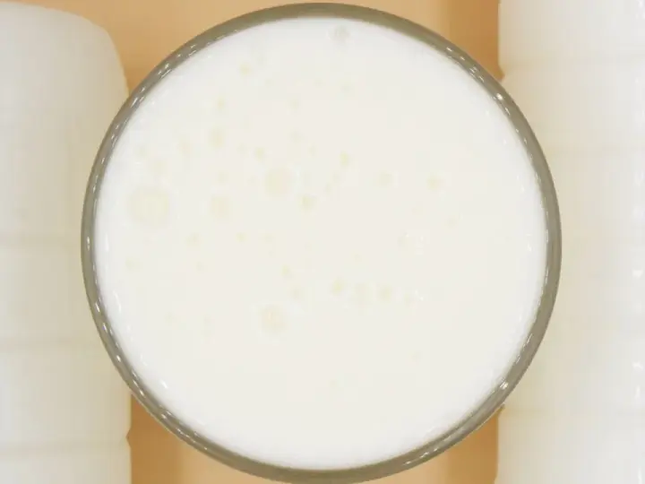 Szklanka pełna pianistego kefiru, otoczona białymi butelkami. Idealny moment, kiedy pić kefir, to teraz!