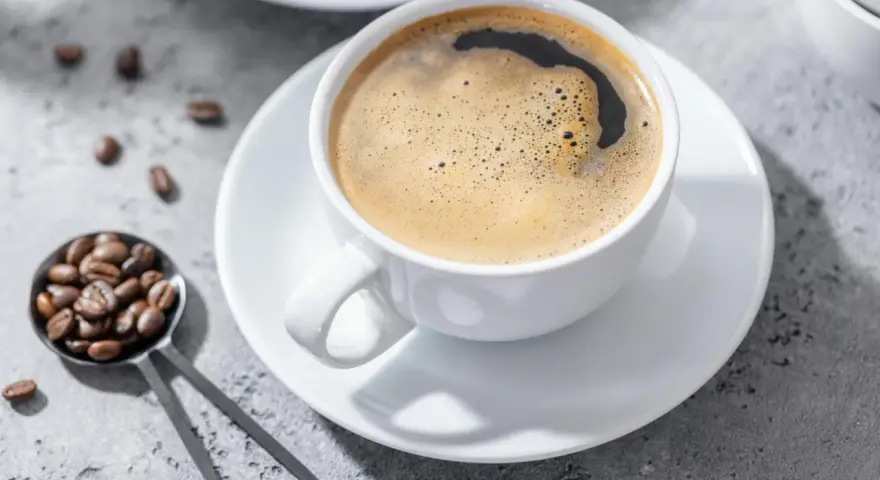 Aromatic coffee in a white cup, with beans on a spoon. Czy kawa jest lekkostrawna? To zależy od sposobu parzenia.
