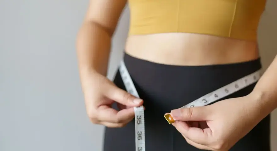 Kobieta mierzy talię centymetrem. Dowiedz się, jak podkręcić metabolizm po 40. i odzyskać formę.