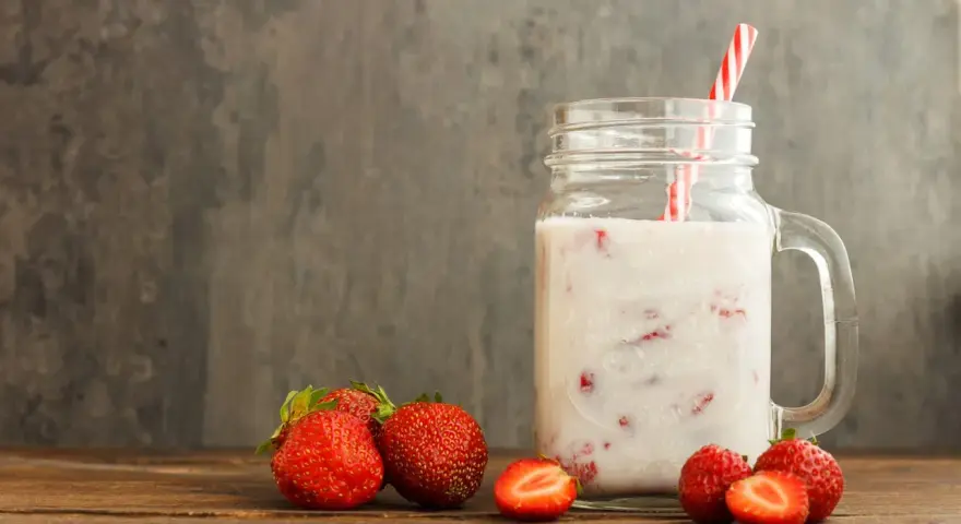 Kefir z truskawkami w słoiku, obok świeże owoce. Niska wartość indeksu glikemicznego sprawia, że to zdrowa przekąska.