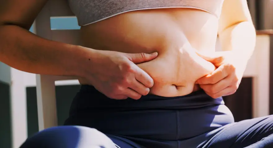 Kobieta chwyta fałd tłuszczu na brzuchu, zastanawiając się, jak schudnąć 4 kg.