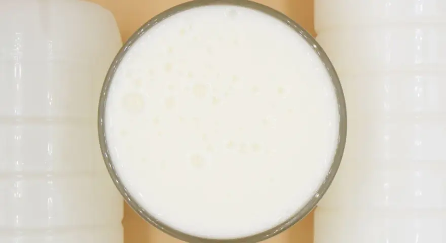Szklanka pełna pianistego kefiru, otoczona białymi butelkami. Idealny moment, kiedy pić kefir, to teraz!