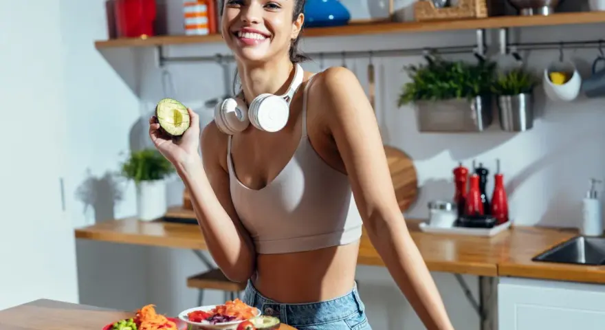 Uśmiechnięta kobieta z awokado w dłoni, przygotowująca posiłki. To inspiracja na dietę odchudzającą dla leniwych jadłospis.