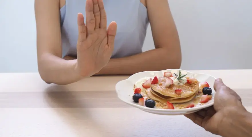 Dłoń odrzuca talerz z naleśnikami i owocami. To symboliczne przedstawienie, jak dieta 1200 kcal efekty po 2 tygodniach motywuje do zdrowych wyborów.