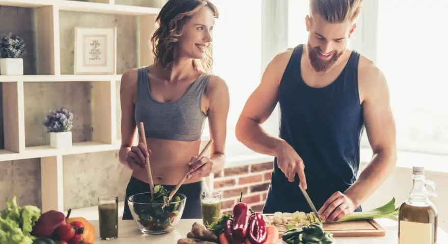Para dieta 3000 kcal jadłospis tygodniowy, para przygotowuje zdrowe posiłki. Ona miesza sałatkę, on kroi warzywa.