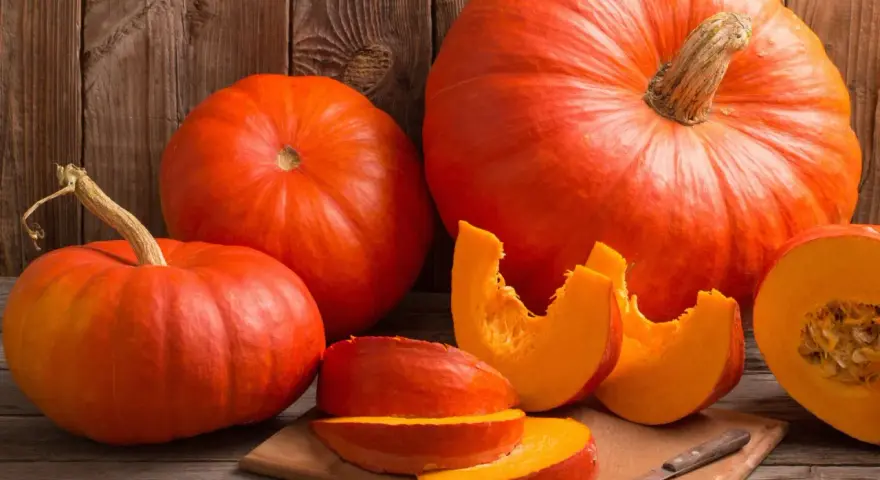 Pomarańczowe dynie, w tym połówka i kawałki na desce, przypominają o ich bogactwie witamin i cennych właściwościach zdrowotnych.