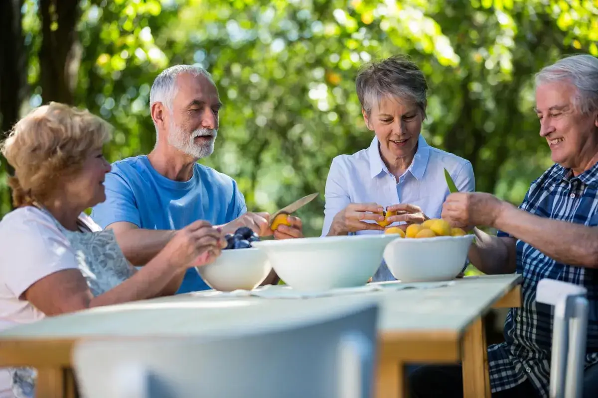 Czterech senior&oacute;w przygotowuje owoce na stole. Zdrowa dieta dla seniora po 80 roku życia to klucz do dobrego samopoczucia.