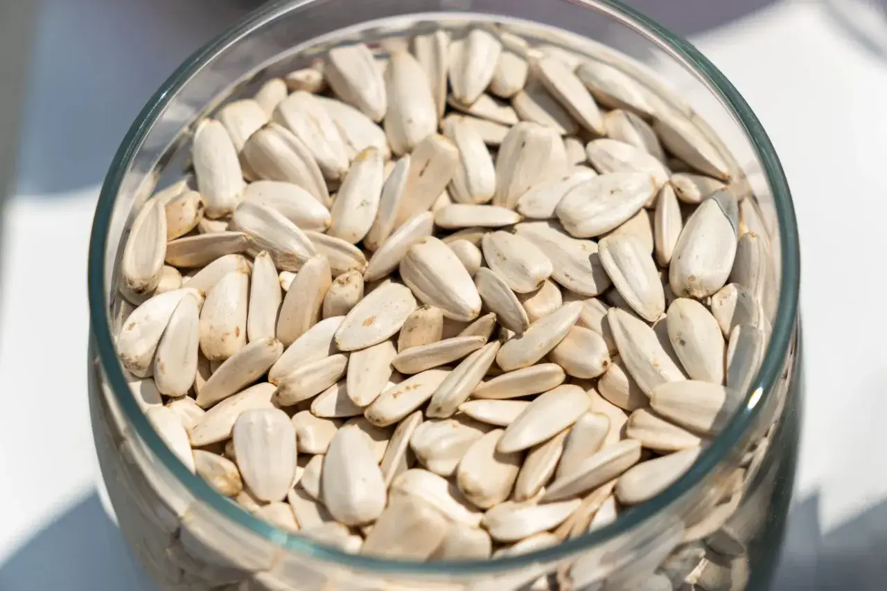 Duża szklana miska pełna białych nasion słonecznika. Uważaj na skutki uboczne jedzenia słonecznika, zwłaszcza jeśli masz wrażliwy żołądek.