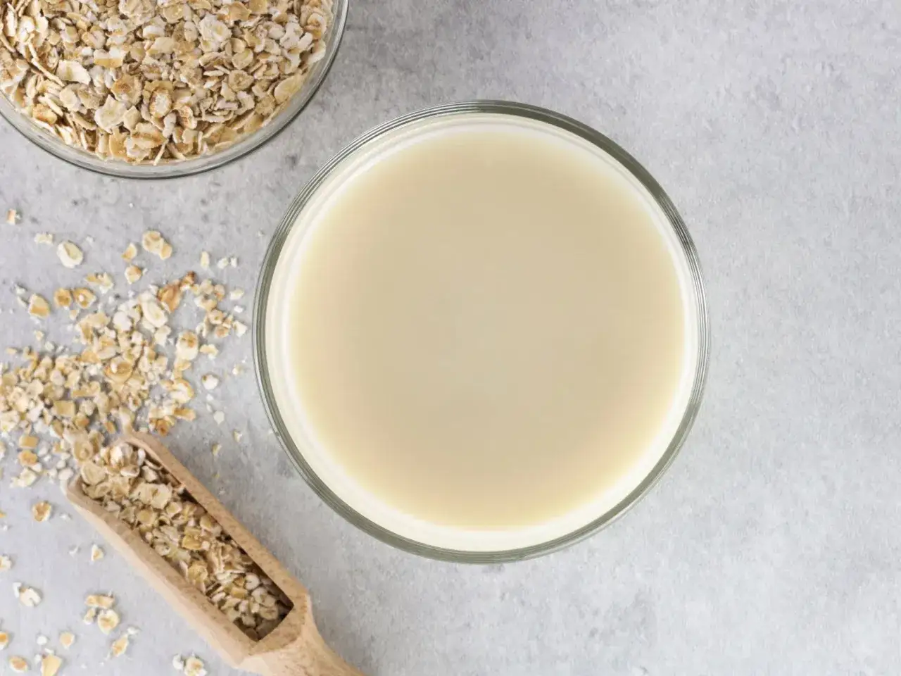 Szklanka mleka owsianego obok płatków owsianych. Czy mleko owsiane ma gluten? Zależy od procesu produkcji.