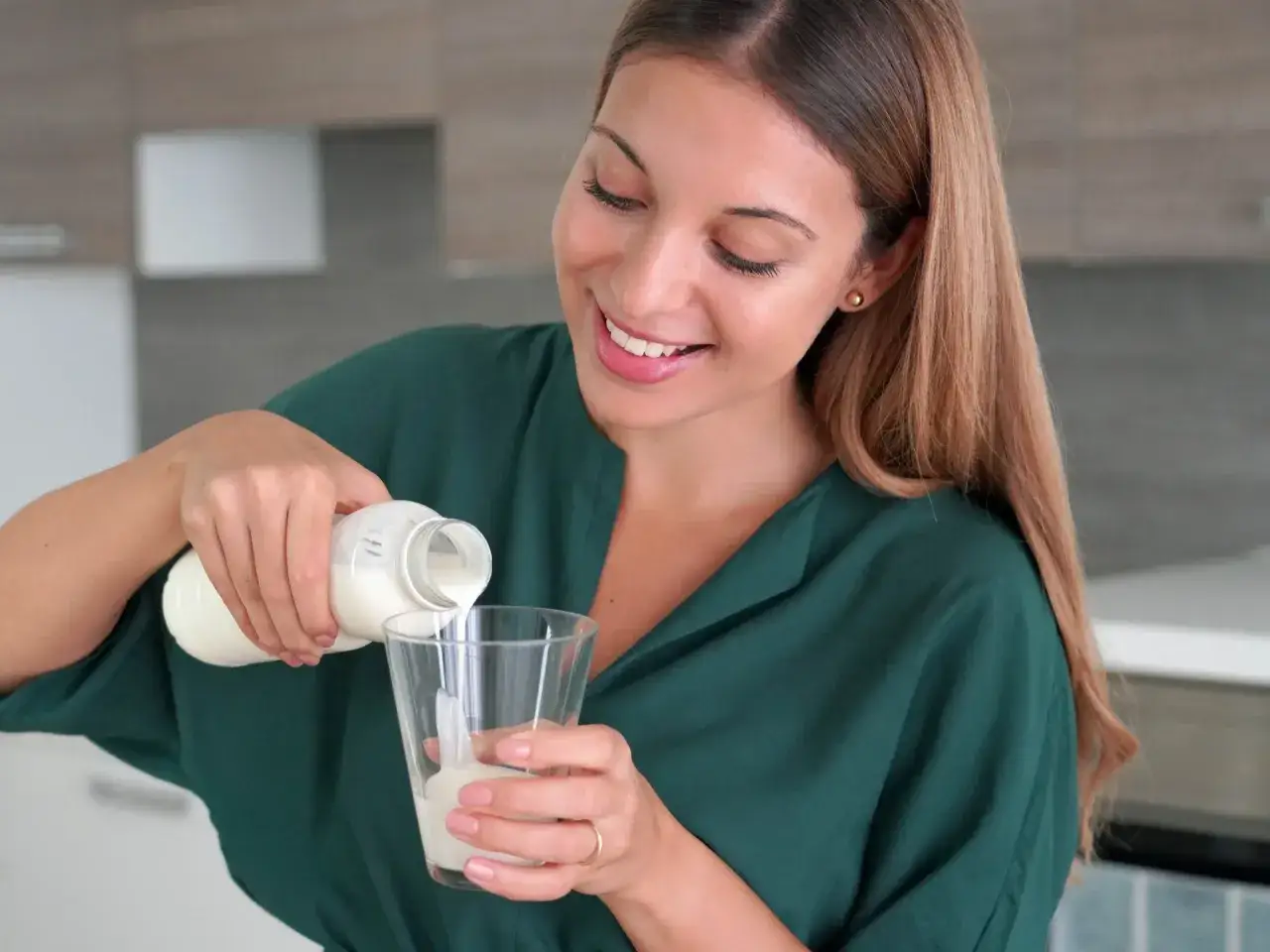 Uśmiechnięta kobieta nalewa kefir do szklanki. Czy kefir jest dobry na odchudzanie? To zdrowy napój, który może wspomóc dietę.