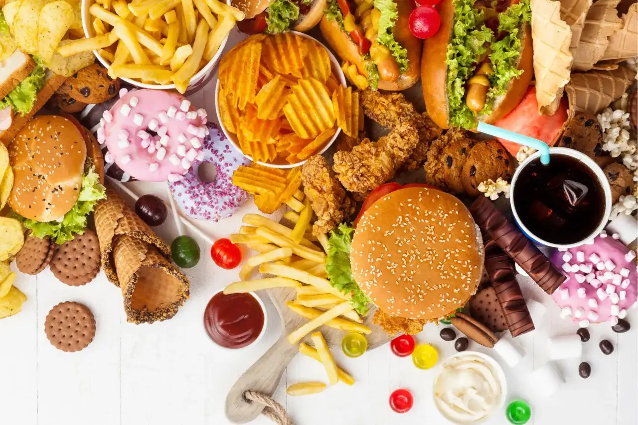 Mnóstwo produktów wysoko przetworzonych: frytki, burgery, hot-dogi, słodycze, ciastka, pączki, chipsy i napoje.