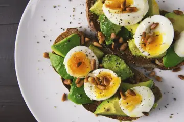 Pyszne tosty z awokado i jajkiem na miękko, idealne do diety 1200 kcal jadłospis. Posypane orzeszkami pinii i pieprzem.
